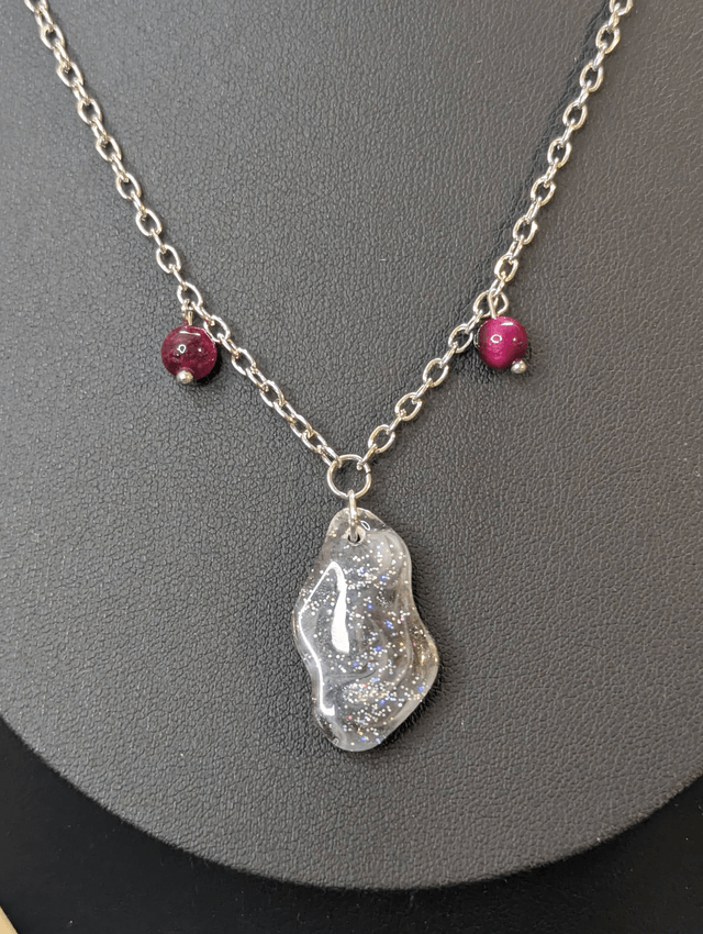 Collier mi long avec une chaine de couleur argent, un pendentif en résine noire et gris pailleté et des perles naturelles rose. 