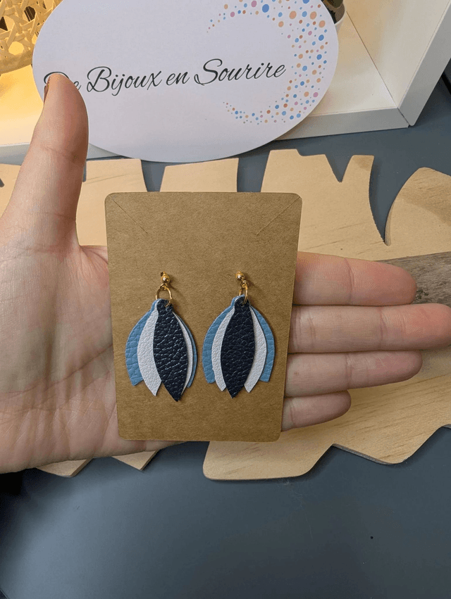 Boucles d'oreilles en cuir en forme de fleur de couleur bleu et blanc le derrière est en tissu enduit, le fermoir clou est en or.