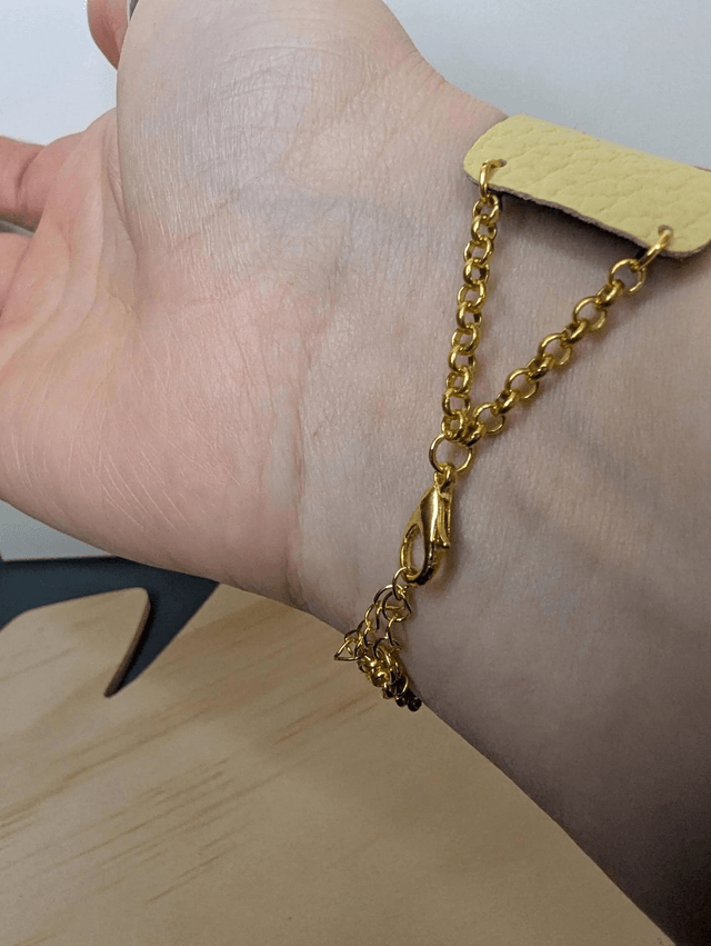 Bracelet manchette en cuir jaune, avec du tissus enduit bleu sombre (résistant), une chaine couleur or. Le fermoir est de couleur or.