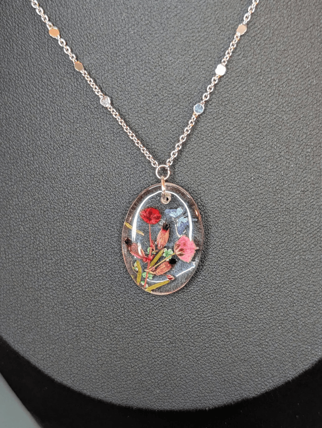 Collier mi long avec une chaine de couleur argent et un pendentif en résine avec des fleurs séchés rouge et rose. 