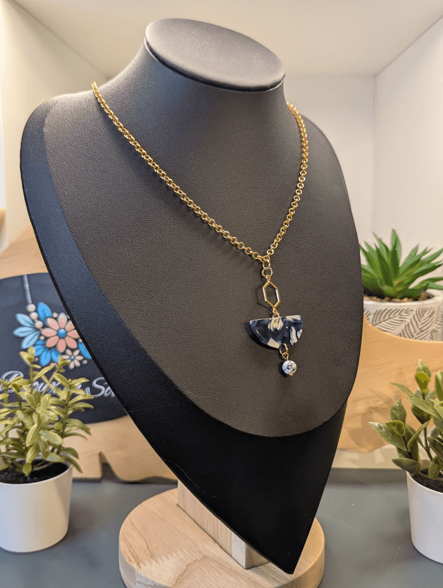 Collier mi long avec une chaine de couleur or et un pendentif en résine bleu et blanc et un pendentif en métal doré.