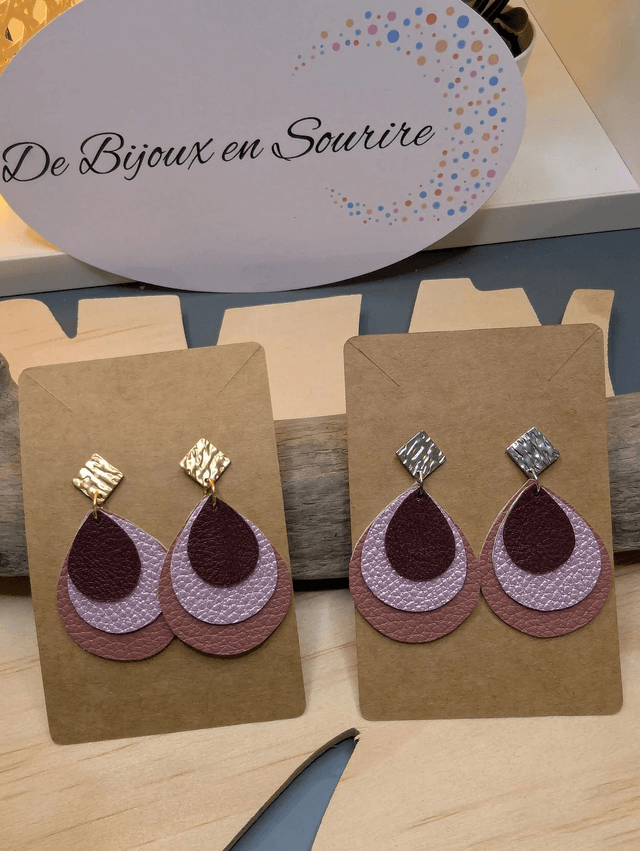 Boucles d'oreilles en cuir en forme de goutte avec un dégradé de rose/violet le derrière est en blanc. Le fermoir en clou carré est de couleur doré.