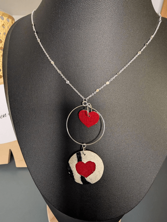 Collier long, sautoir, avec une chaine de couleur argent, un pendentif en cuir et en tissus enduit en forme de rond et de cœur
