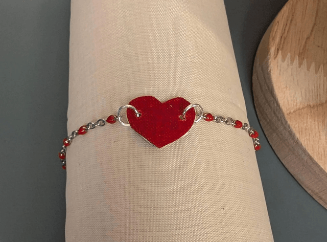 Bracelet en chaine de couleur argent et cœur en cuir et tissus enduit rouge, le fermoir est de couleur argent. 