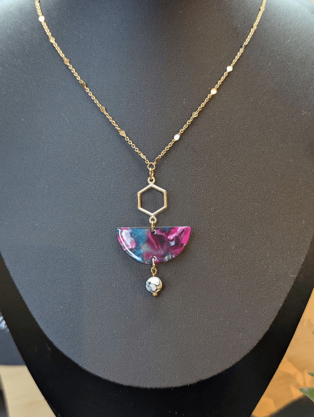 Collier mi long avec une chaine de couleur or et un pendentif en résine rose et bleu et un pendentif en métal doré.