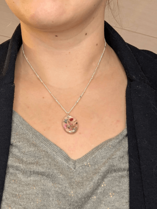 Collier mi long avec une chaine de couleur argent et un pendentif en résine avec des fleurs séchés rouge et rose. 