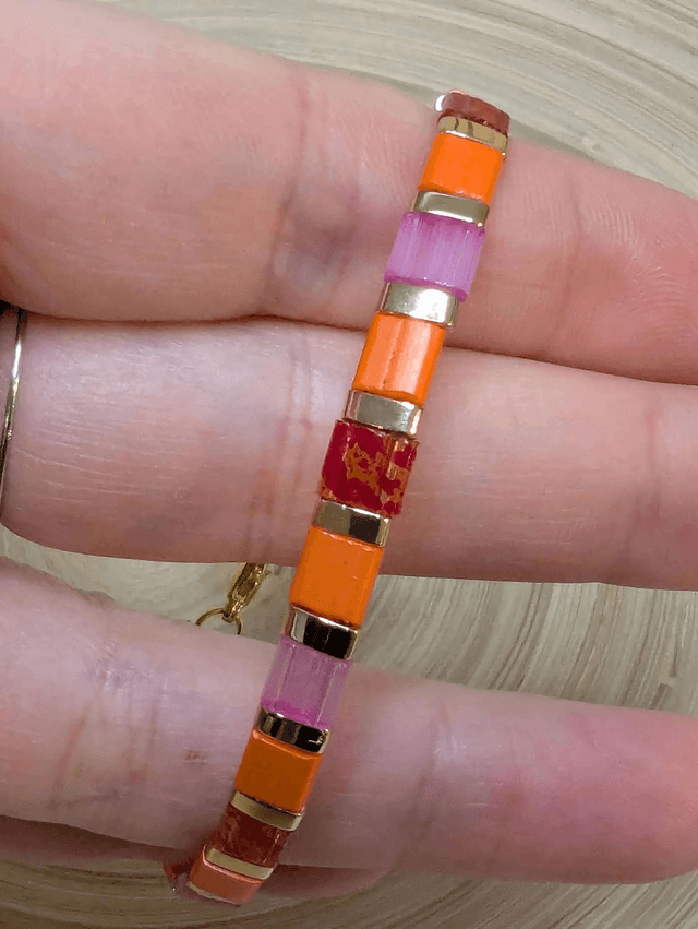Bracelet avec des perles plate en verre rose, orange et des petites en métal doré. Le fermoir et la chaine fermoir sont en or.