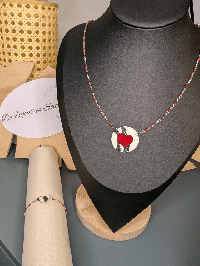Bracelet en chaine de couleur argent et cœur en cuir et tissus enduit rouge, le fermoir est de couleur argent. 