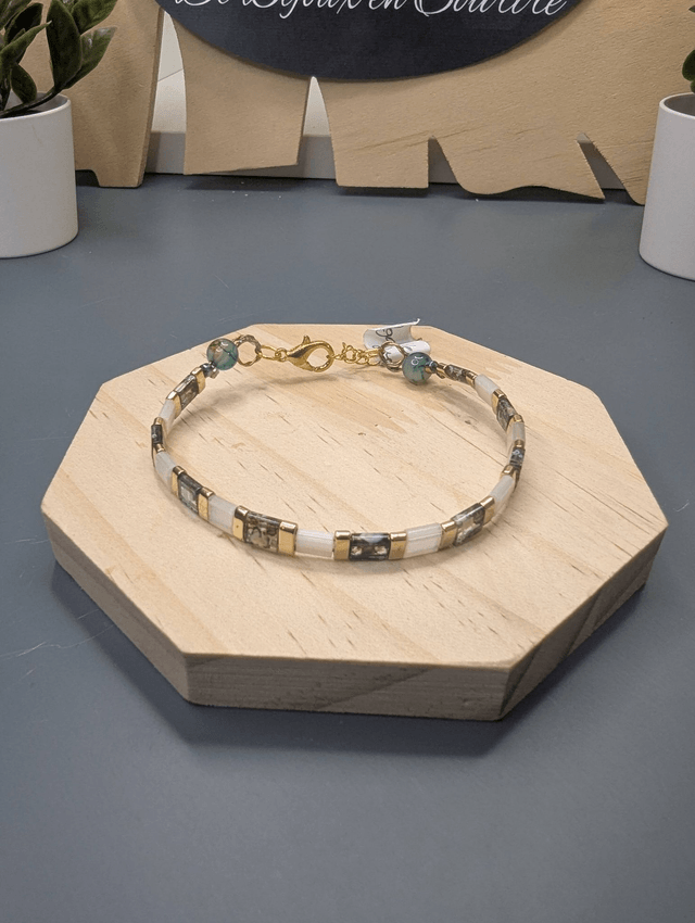 Bracelet avec des perles plate en verre blanches et verts d'eau et des perles en métal doré. Le fermoir et la chaine fermoir sont de couleur or.