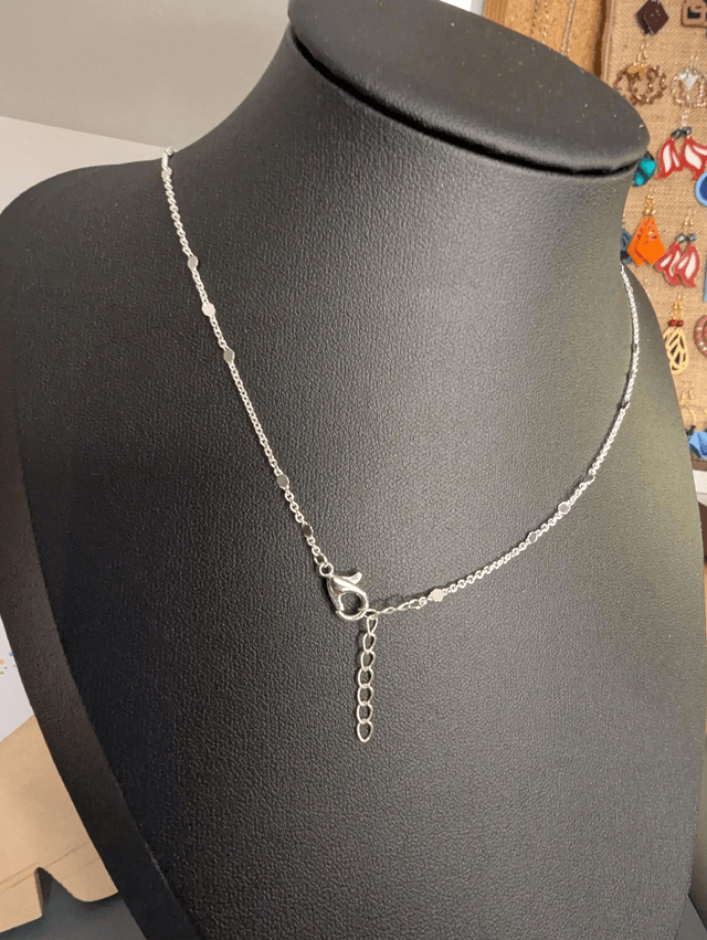 Collier long, sautoir, avec une chaine de couleur argent, un pendentif en cuir et en tissus enduit en forme de rond et de cœur