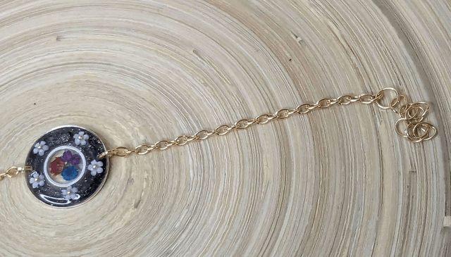 Bracelet avec une chaine de couleur or, le pendentif est en résine noir avec des fleurs séchés, le fermoir est en or. 