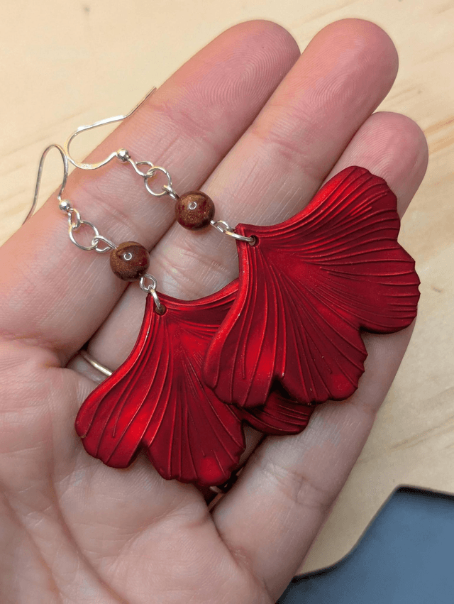 Boucles d'oreilles pendentifs en forme de feuilles, de couleur rouge métallisé avec des perles de cloisonne rouge et marron. 