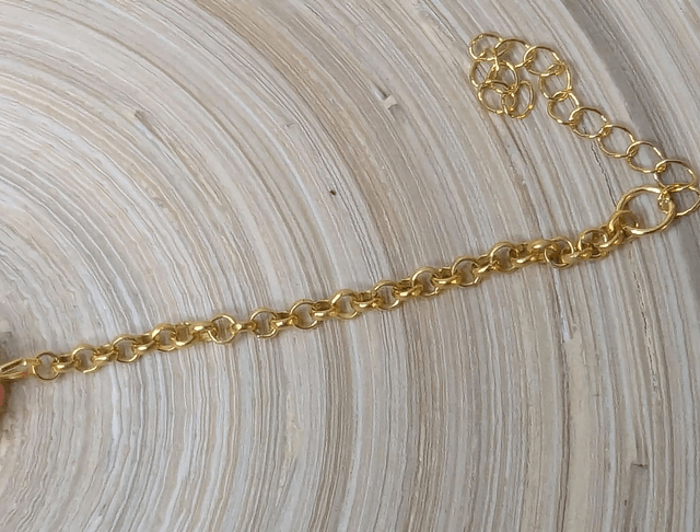Bracelet avec une chaine de couleur or et un pendentif en résine rose transparent, motif fleur, le fermoir est en or.