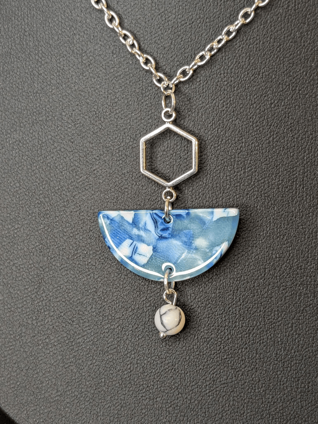 Collier mi long avec une chaine de couleur argent et un pendentif en résine bleu et blanc, et un pendentif en métal argenté. 