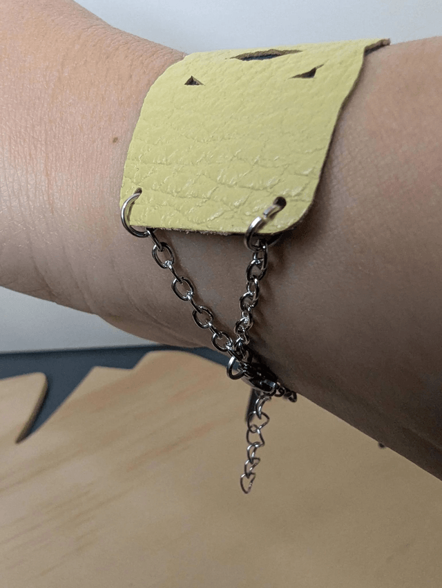 Bracelet manchette en cuir jaune, avec du tissus enduit bleu sombre (résistant), avec une chaine en argent. Le fermoir est de couleur argent.