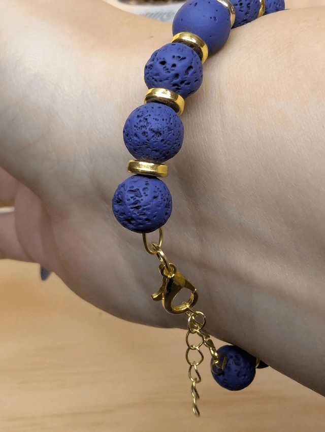 Bracelet en pierre de lave bleu foncé, avec des perles d'espacement doré. Le fermoir et la chaine fermoir sont de couleur or.