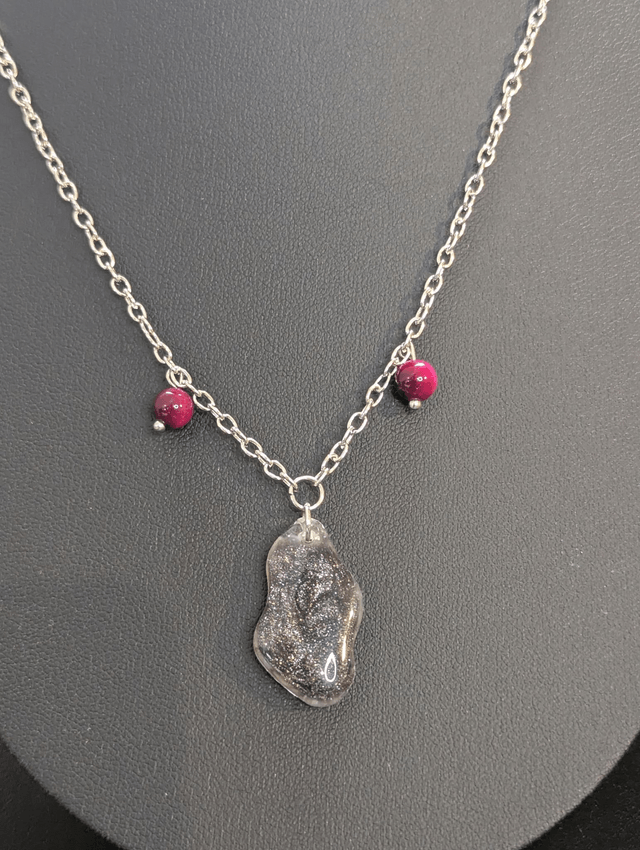Collier mi long avec une chaine de couleur argent, un pendentif en résine noire et gris pailleté et des perles naturelles rose. 