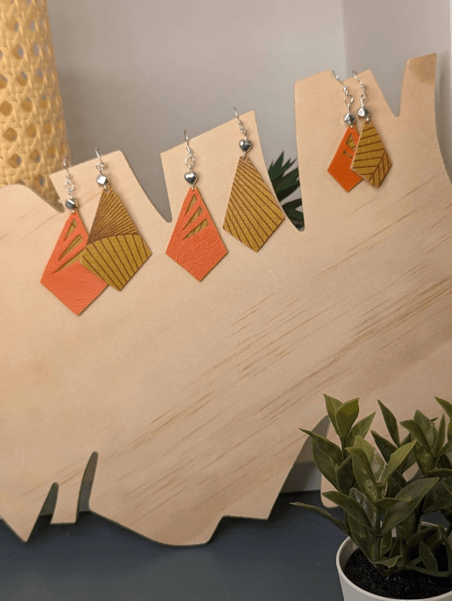 Boucles d'oreilles longue en similicuir orange et tissus enduit, avec des perles métalliques de forme géométrique, le fermoir est en argent. 