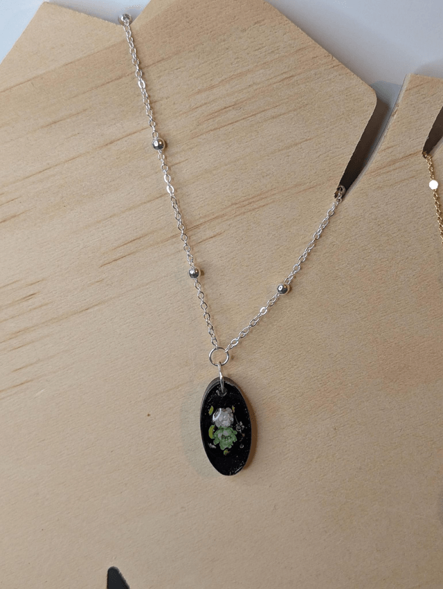 Collier mi long avec une chaine de couleur argent et un pendentif en résine noire avec des fleurs séchés. 