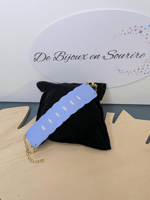 Bracelet manchette en cuir bleu lisse, avec du tissus enduit blanc (résistant), une chaine dorée. Le fermoir est de couleur or. 