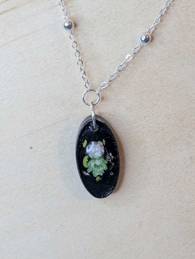 Collier mi long avec une chaine de couleur argent et un pendentif en résine noire avec des fleurs séchés. 