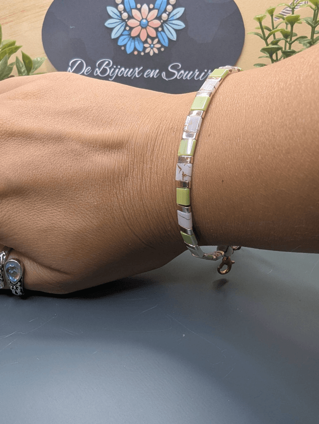 Bracelet avec des perles plate en verre blanches et vertes et des perles en métal doré. Le fermoir et la chaine fermoir sont de couleur or.