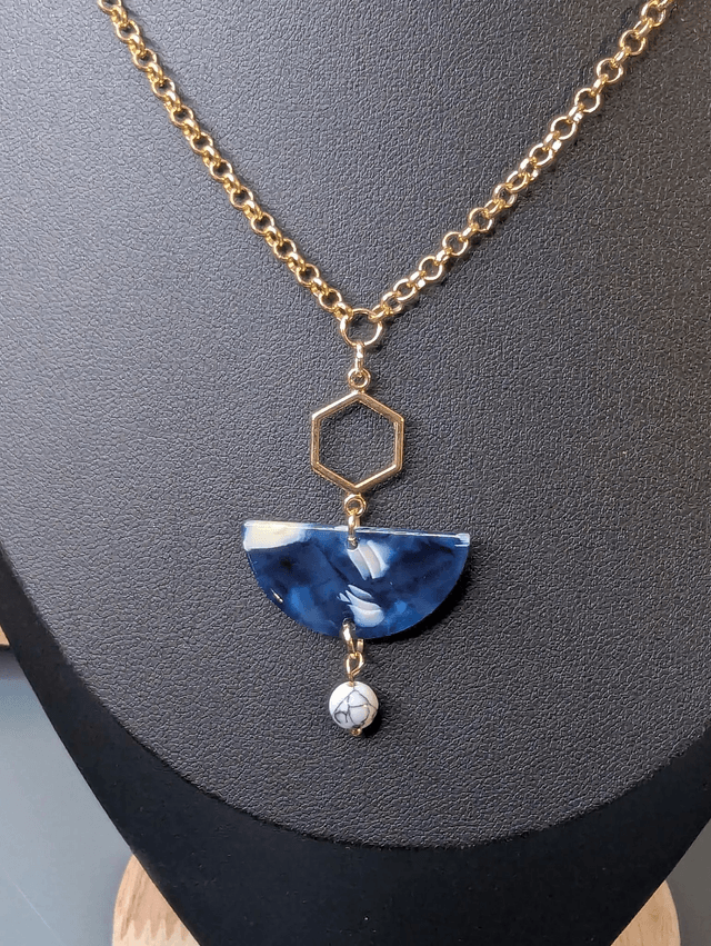 Collier mi long avec une chaine de couleur or et un pendentif en résine bleu et blanc, et un pendentif en métal doré. 