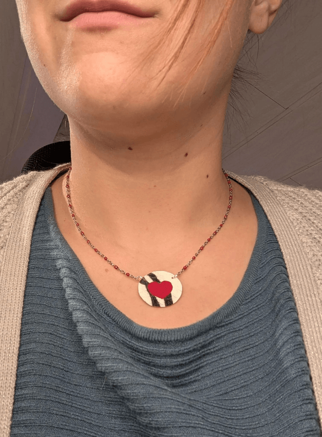 Collier mi long avec une chaine de couleur argent et rouge, avec un pendentif en cuir et en tissus enduit en forme de rond et de cœur. 