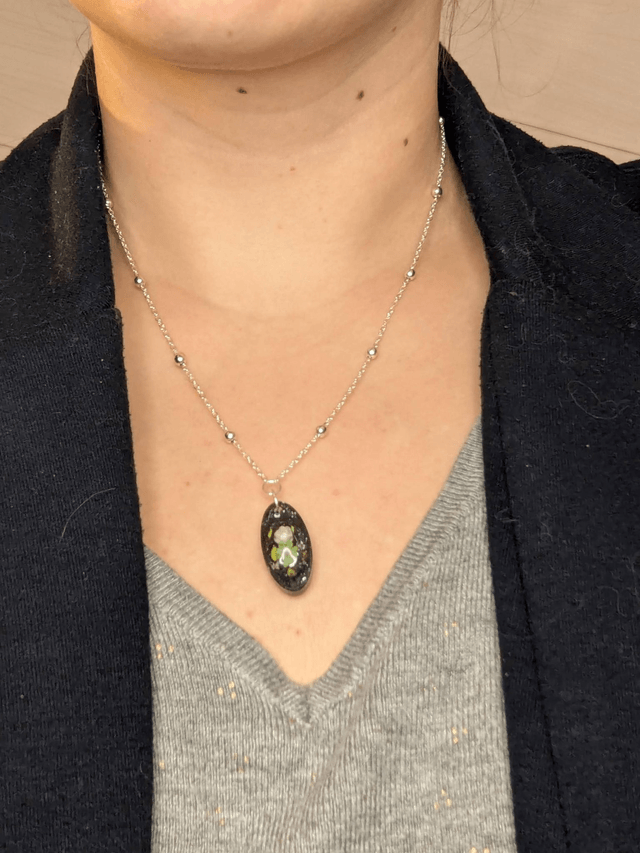 Collier mi long avec une chaine de couleur argent et un pendentif en résine noire avec des fleurs séchés. 