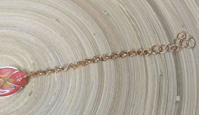 Bracelet ave une chaine de couleur or, pendentif en résine rose et jaune avec des petites fleurs blanches, le fermoir est or.
