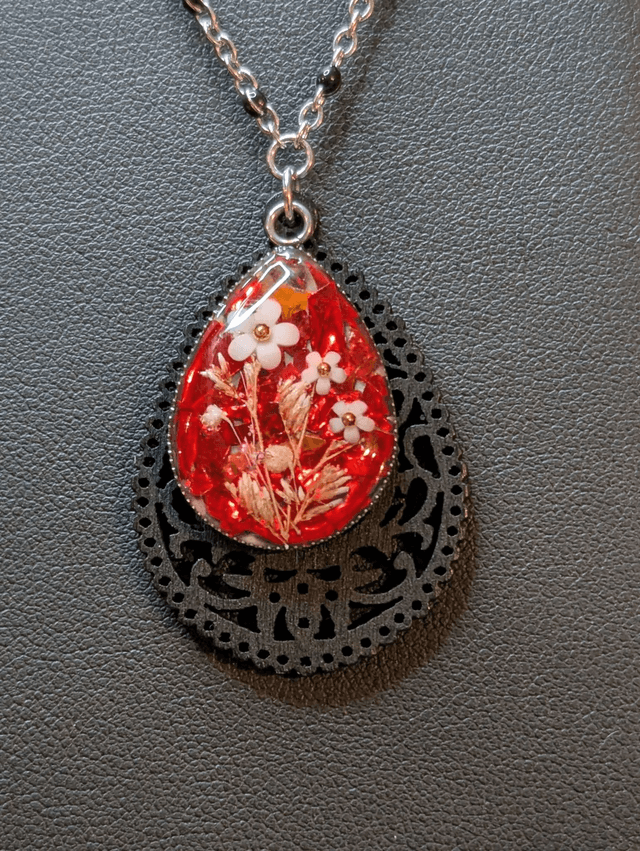 Collier sautoir long avec un pendentif en bois noir et un pendentif en résine rouge, fleurs blanche, chaine en argent. 