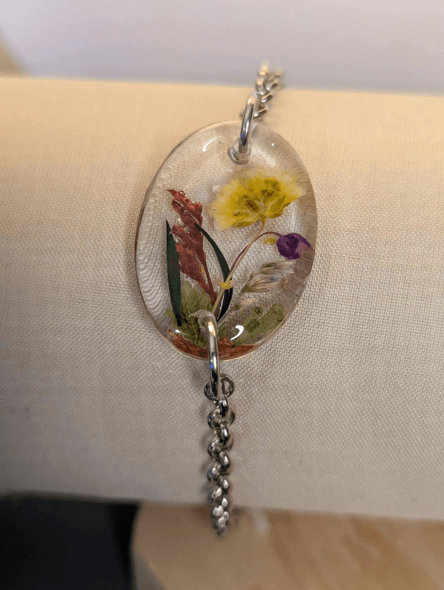  Bracelet avec une chaine de couleur argent et un pendentif en résine avec des fleurs séchés jaune, le fermoir est en argent. 