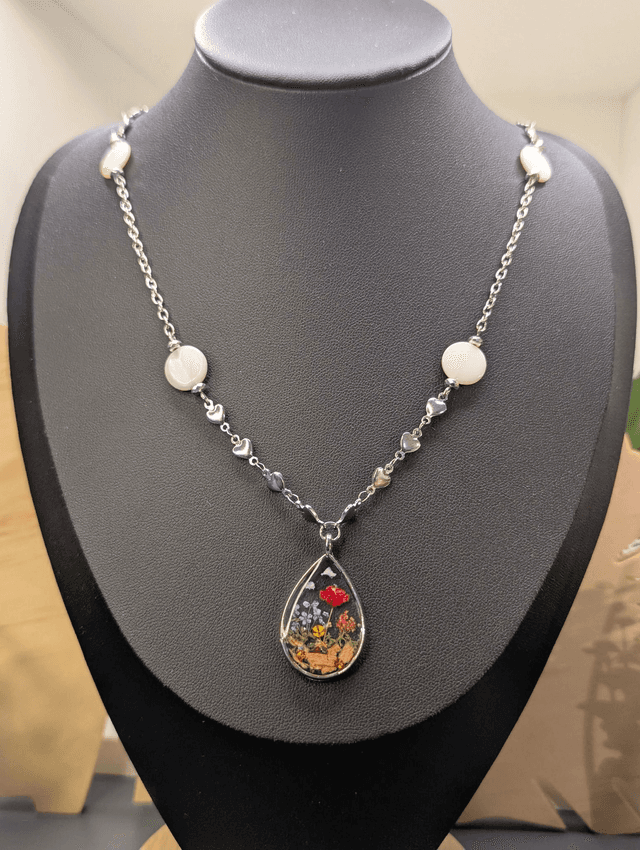 Collier mi long avec deux chaines de couleurs argent, des perles de nacre et un pendentif en résine avec fleurs séchés. 