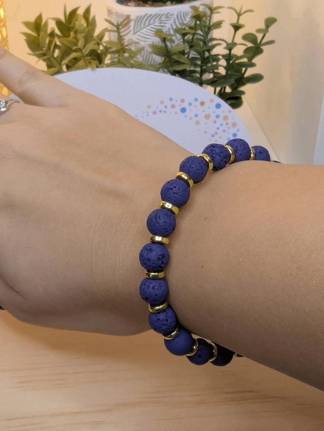 Bracelet en pierre de lave bleu foncé, avec des perles d&#039;espacement doré. Le fermoir et la chaine fermoir sont de couleur or.