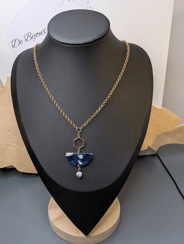 Collier mi long avec une chaine de couleur or et un pendentif en résine bleu et blanc, et un pendentif en métal doré. 