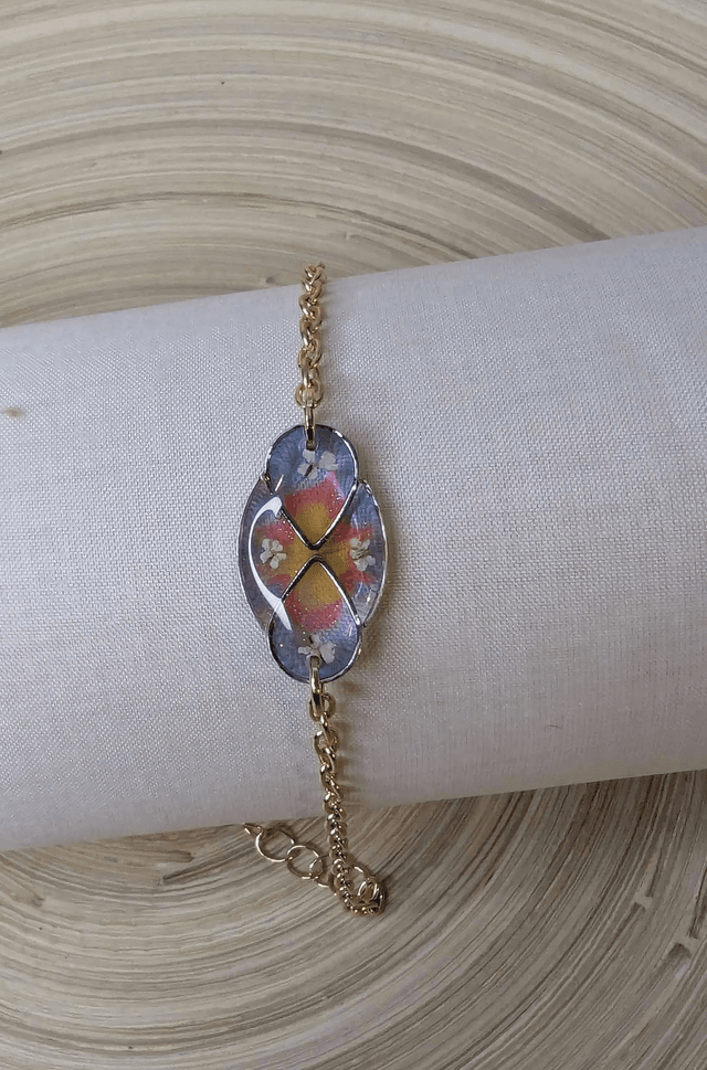 Bracelet avec une chaine de couleur or, pendentif en résine bleu, rose et jaune avec des petites fleurs blanches, le fermoir est en or.