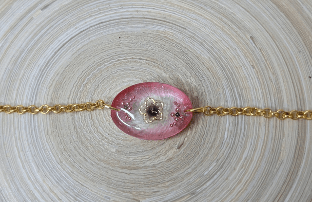 Bracelet avec une chaine de couleur or et un pendentif en résine rose transparent, motif fleur, le fermoir est en or.