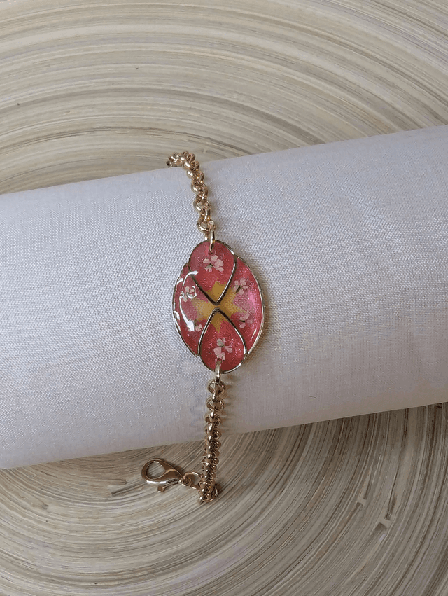 Bracelet ave une chaine de couleur or, pendentif en résine rose et jaune avec des petites fleurs blanches, le fermoir est or.