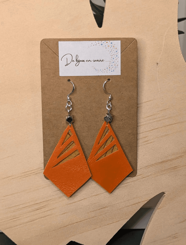 Boucles d&#039;oreilles longue en similicuir orange et tissus enduit, avec des perles métalliques de forme géométrique, le fermoir est en argent. 